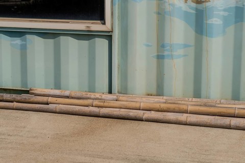Weathered cracked bamboo poles laying on concrete driveway in front of aluminum building wall in