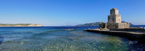 An old stone tower on a coast with crystal clear sea water under a wide blue sky, octagonal