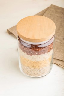 Glass jar with different kinds of rice poured in layers on white background. side view, close up.