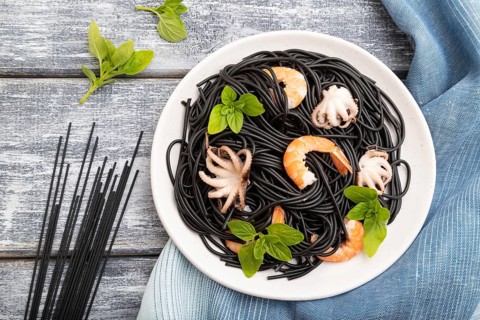 Black cuttlefish ink pasta with shrimps or prawns and small octopuses on gray wooden background and