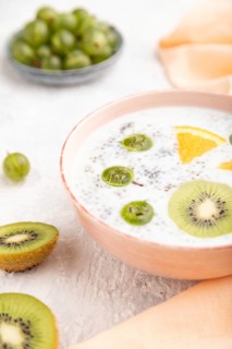 Yogurt with kiwi, gooseberry, chia in ceramic bowl on gray concrete background and orange linen