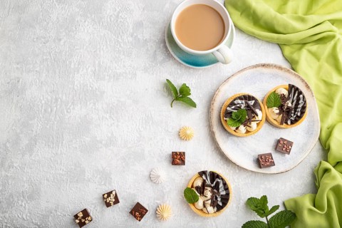 Sweet tartlets with chocolate and cheese cream with cup of coffee on a gray concrete background and