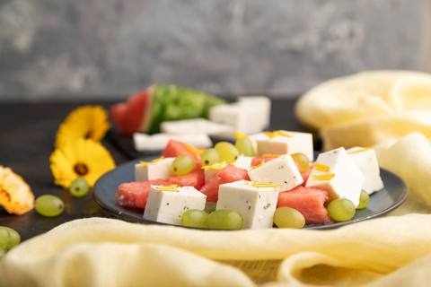 Vegetarian salad with watermelon, feta cheese, and grapes on blue ceramic plate on black concrete