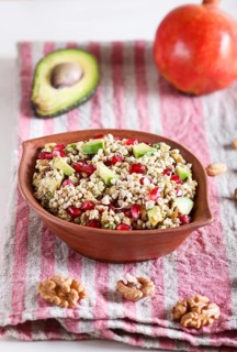 Salad of germinated buckwheat, avocado, walnut and pomegranate seeds in clay plate on white wooden