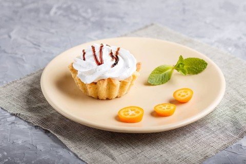 Cake with whipped egg cream on a light brown plate with kumquat slices and mint leaves on a gray