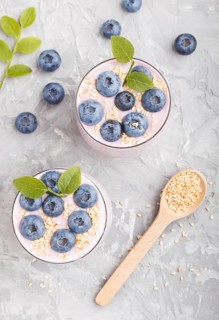 Yoghurt with blueberry and sesame in a glass and wooden spoon on gray concrete background. top
