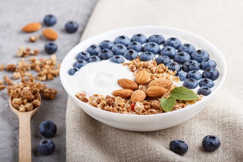 Yoghurt with blueberry, granola and almond in white plate with wooden spoon on gray concrete