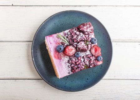 Berry cake with milk cream and blueberry jam on blue ceramic plate on a white wooden background.