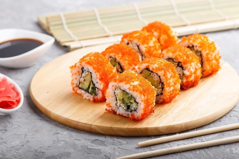 Japanese maki sushi rolls with flying fish roe, chopsticks, soy sauce and marinated ginger on
