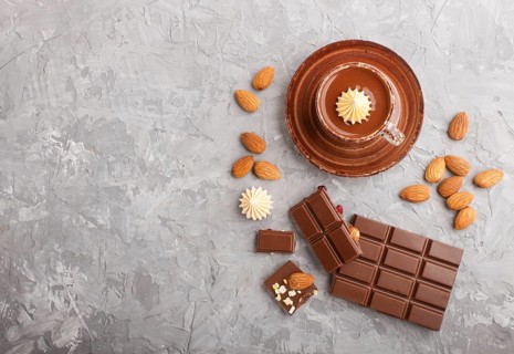 Cup of hot chocolate and pieces of milk chocolate with almonds on a gray concrete background. Flat