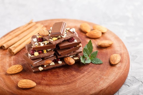 A pieces of milk chocolate with almonds and dried fruits on a brown wooden board on a gray concrete