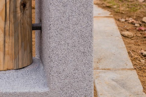 Closeup of bottom of unpainted wooden post held in concrete footing with large threaded bolts in