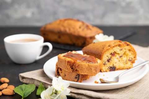 Homemade cake with raisins, almonds, soft caramel and a cup of coffee on a black concrete