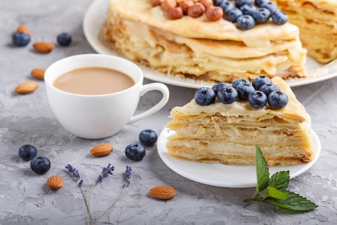 Homemade layered Napoleon cake with milk cream. Decorated with blueberry, almonds, walnuts,