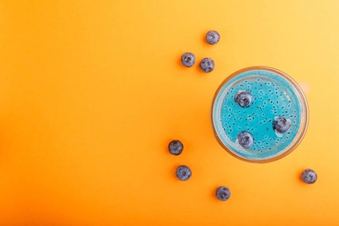 Glass of blueberry blue colored drink with basil seeds on orange background. Morninig, spring,
