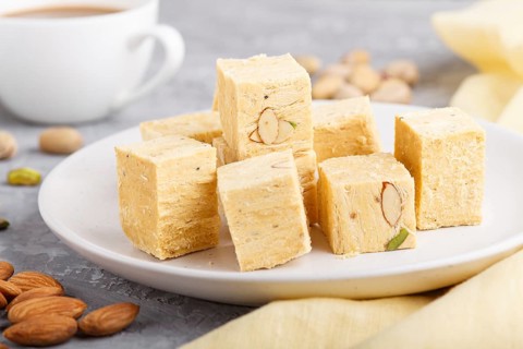 Traditional indian candy soan papdi in white plate with almond, pistache and a cup of coffee on a