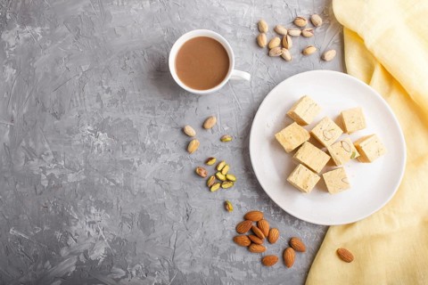 Traditional indian candy soan papdi in white plate with almond, pistache and a cup of coffee on a