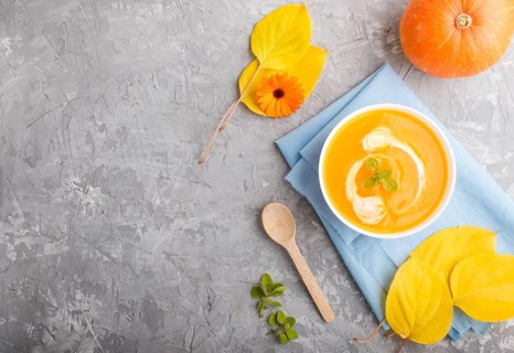Traditional pumpkin cream soup with in white bowl on a gray concrete background with blue napkin.