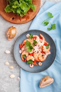 Boiled shrimps or prawns and small octopuses with herbs on a blue ceramic plate on a gray concrete