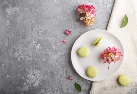 Green macarons or macaroons cakes on white ceramic plate on a gray concrete background and linen