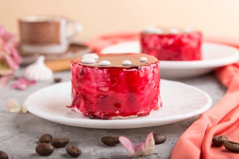 Red cake with souffle cream with cup of coffee on a gray concrete background and red textile. side