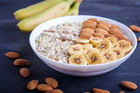 A plate with muesli, almonds, banana, sliced persimmon on a black wooden background. close up. copy