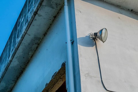 Flood light mounted on outside wall of abandoned concrete building with blue sky in background in