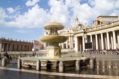 View of a fountain in St Peter's Square in the Vatican in front of the basilica under a cloudy sky