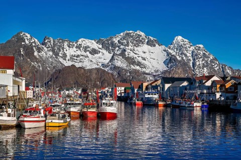 Bunte Boote und Gebaeude vor schneebedeckten Bergen in einem Hafen, Im Hafen von Henningsvaer auf