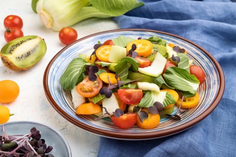 Vegetarian salad of pac choi cabbage, kiwi, tomatoes, kumquat, microgreen sprouts on a white