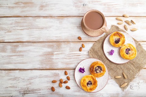 Small cheesecakes with jam and almonds with cup of coffee on a white wooden background and linen