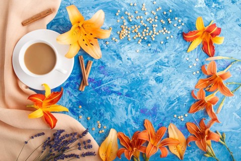 Orange day-lily and lavender flowers and a cup of coffee on a blue concrete background, with orange