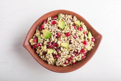 Salad of germinated buckwheat, avocado, walnut and pomegranate seeds in clay plate on white wooden