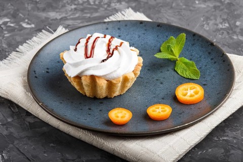 Cake with whipped egg cream on a blue ceramic plate with kumquat slices and mint leaves on a black