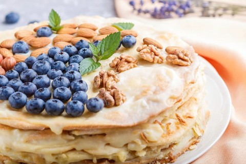 Homemade layered Napoleon cake with milk cream. Decorated with blueberry, almonds, walnuts,