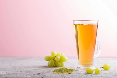 Glass of green grape juice on a gray and pink background. Morninig, spring, healthy drink concept.