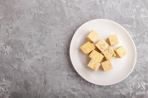Traditional indian candy soan papdi in white plate with almond and pistache on a gray concrete