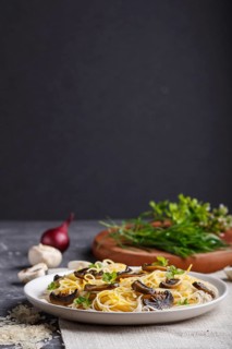 Rice noodles with champignons mushrooms, egg sauce and oregano on white ceramic plate on a black