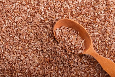 Texture of unpolished brown rice with wooden spoon. Top view, flat lay, close up, macro. Natural
