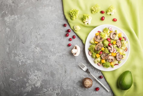 Vegetarian salad from romanesco cabbage, champignons, cranberry, avocado and pumpkin on a gray