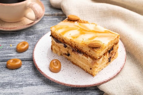 Honey cake with milk cream, caramel, almonds and a cup of coffee on a gray wooden background and