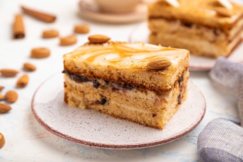 Honey cake with milk cream, caramel, almonds and a cup of coffee on a white concrete background and