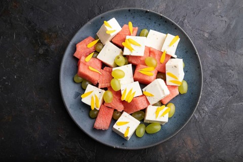 Vegetarian salad with watermelon, feta cheese, and grapes on blue ceramic plate on black concrete