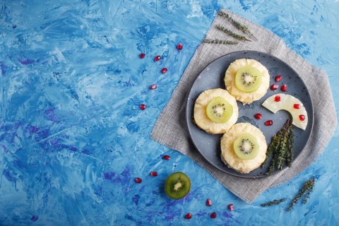 Pieces of baked pork with pineapple, cheese and kiwi on blue background, top view, copy space
