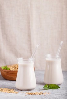 Organic non dairy oats milk in glass and wooden plate with oats seeds on a gray concrete background