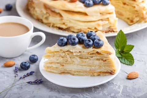 Homemade layered Napoleon cake with milk cream. Decorated with blueberry, almonds, walnuts,