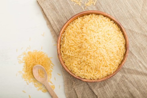 Wooden bowl with raw golden rice and wooden spoon on a white wooden background and linen textile.