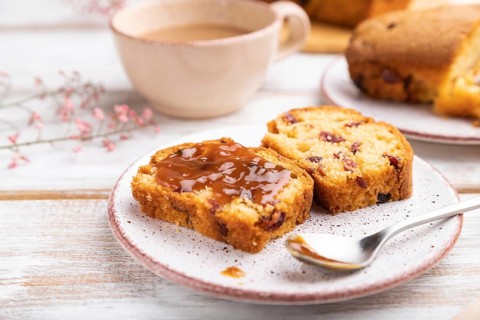 Homemade cake with raisins, almonds, soft caramel and a cup of coffee on a white wooden background.