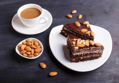 Chocolate cake with caramel, peanuts and almonds on a black wooden background. cup of coffee, close