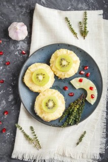 Pieces of baked pork with pineapple, cheese and kiwi on black background, top view